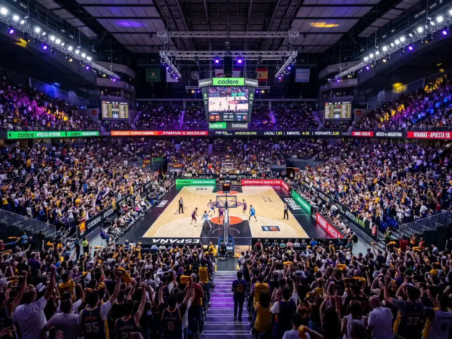 Pabellón NBA lleno de aficionados con pantallas mostrando cuotas de apuestas en directo
