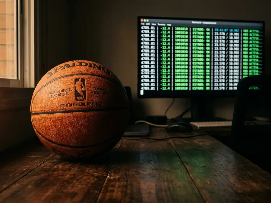 Tipos de apuestas NBA: balón de baloncesto junto a una pantalla con cuotas y mercados de apuestas